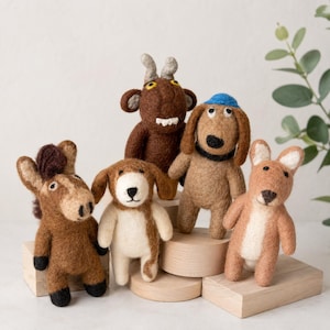 May include: A collection of five handmade felt animal figurines, including a horse, two dogs, a goat, and a kangaroo. The toys are primarily brown and tan, with white and black accents. The dog has a blue hat. The toys are displayed on wooden platforms.
