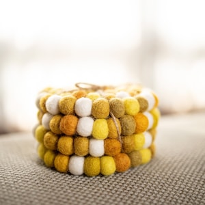 May include: A set of four yellow, white, and orange felt coasters tied together with twine. The coasters are made of small, round felt balls.