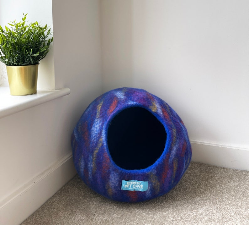 May include: A blue and purple felt cat bed with a round shape and a large opening. The bed has a blue label with the text "Everest Pet Cave".