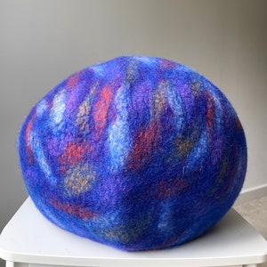 May include: A blue, purple, and orange felted wool ball. The ball is round and has a soft, fuzzy texture.