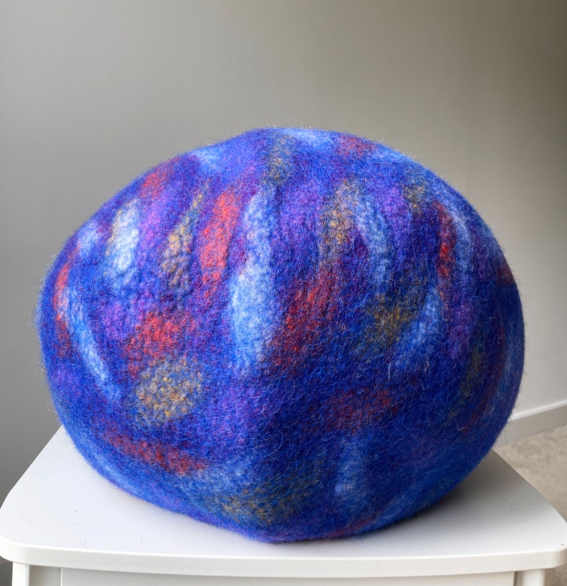 May include: A blue, purple, and orange felted wool ball. The ball is round and has a soft, fuzzy texture.