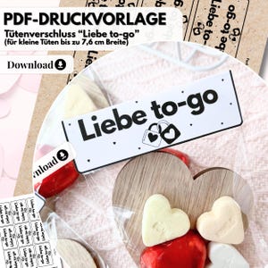 May include: A clear cellophane bag containing heart-shaped candies and wooden hearts. A white label with the text "Liebe to-go" and a lock icon is attached to the bag. The image also includes text that says "PDF-DRUCKVORLAGE" and "Download".