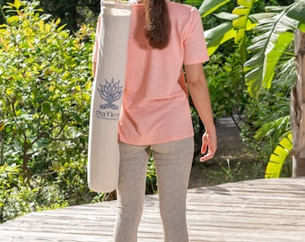 May include: A person wearing a pink t-shirt and grey leggings is holding a white yoga mat bag with the text "chaYkra" and "free flowing energy" printed on it.
