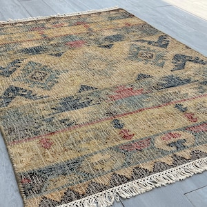 Pode incluir: Um tapete tecido com um padrão geométrico em tons de azul, vermelho e bege. O tapete tem uma borda de franjas.