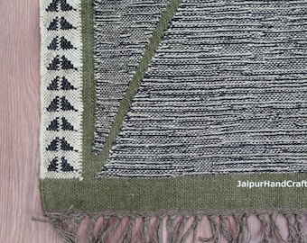 May include: Close-up of a woven rug with a geometric design. The rug features a black and white striped pattern with a green border and fringe. A section of the rug has a triangle design. The text "JaipurHandCraftsShop" is visible.