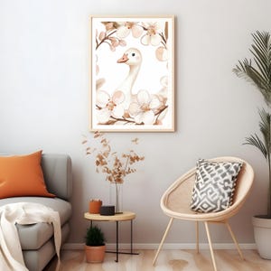 Puede incluir: Una ilustraci&oacute;n de acuarela de un ganso blanco con un pico y patas rosas, rodeado de delicadas flores rosas y blancas. La ilustraci&oacute;n est&aacute; enmarcada en un marco de madera claro y cuelga de una pared blanca.