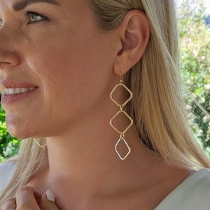 May include: Gold tone earrings and bracelet with a geometric diamond shape design. The earrings are long and dangle. The bracelet is a chain style.