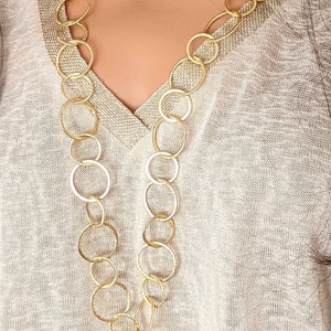 Può includere: Una collana a catena dorata con grandi maglie rotonde. La collana è indossata da una persona con un maglione marrone chiaro.