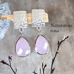Könnte beinhalten: Ein Paar Ohrclips mit einem rechteckigen, silberfarbenen Oberteil mit gehämmertem Muster, verbunden mit einem facettierten, tropfenförmigen Anhänger aus hellrosa Naturstein. Der Text "Clips", "Naturstein rosa" und "Edel-und-Kreativ" ist zu sehen.