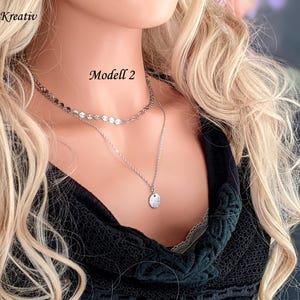 Op de afbeelding: Een zilverkleurige gelaagde ketting bestaande uit een korte ketting met kleine platte ronde schakels en een langere ketting met een kleine ronde hanger. De tekst Edel-und-Kreativ en Modell 2 is zichtbaar. De ketting wordt gedragen over een zwart bovenstuk.