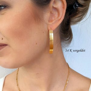 May include: A gold-coloured hoop earring with a flat, wide band design. The earring features a brushed metal texture and a smooth finish. The text 14 K vergoldet and Edel-und-Kreativ is visible on the image, indicating the gold-plated material.