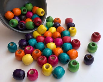 Puede incluir: Una colección de cuentas de madera coloridas en varios tonos, incluyendo rojo, amarillo, verde y azul, derramándose de un cuenco gris. Las cuentas son redondas con un agujero en el centro, adecuadas para manualidades o joyería.