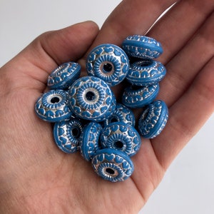 May include: A collection of blue and silver decorative beads with a floral design. The beads are round and have a hole in the centre.