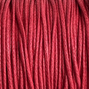 May include: Close-up of a spool of red waxed cotton cord. The cord is tightly wound and has a smooth, polished finish.