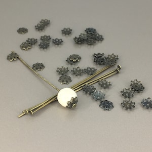 May include: A collection of antique gold-toned metal flower-shaped bead caps with a white bead and metal pins.