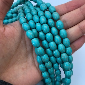 May include: A strand of turquoise oval beads with a marbled pattern. The beads are a light blue colour with darker blue veins running through them.