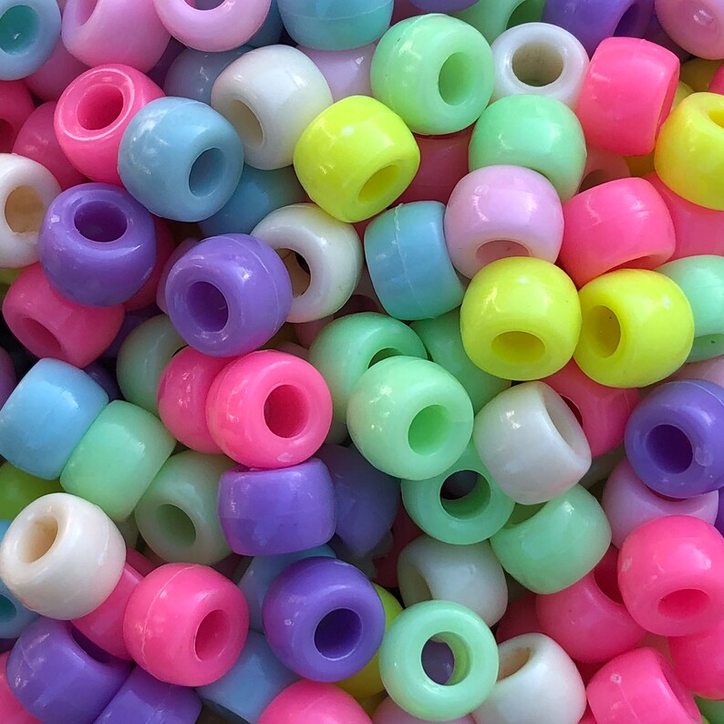 Puede incluir: Primer plano de un mont&oacute;n de cuentas de poni de colores. Las cuentas son de varios colores pastel, incluyendo rosa, morado, azul, verde, amarillo y blanco. Cada cuenta es cil&iacute;ndrica con un agujero grande en el centro.