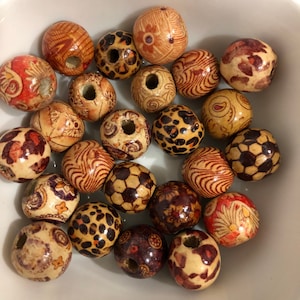 May include: A selection of wooden beads with diverse patterns and sizes. The beads display designs like floral, leopard print, and geometric shapes. Colours include natural wood tones, red, brown, and black. Each bead has a hole for threading.