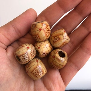 May include: A close-up of six wooden beads with a geometric pattern and red accents. The beads are in a hand, and they are all different sizes.