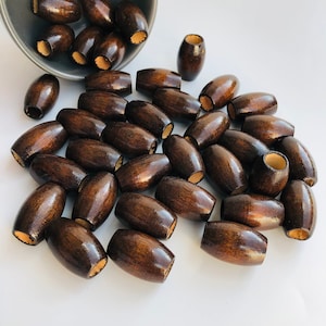 May include: A large group of dark brown wooden beads, scattered on a white surface. The beads are oval shaped and have a smooth, polished finish.