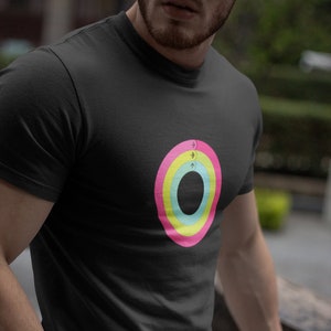 Puede incluir: Una camiseta negra con un diseño circular de colores. El círculo tiene cuatro anillos concéntricos en rosa, amarillo, verde y azul. El centro del círculo es negro. Hay flechas y una luna creciente en el círculo.