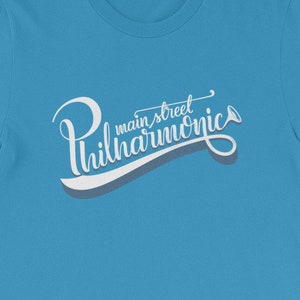 May include: A light blue t-shirt with a white graphic that says "Main Street Philharmonic" in a stylized font with a musical note.