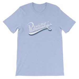 May include: Light blue t-shirt with a white graphic that says "main street philharmonics" in a stylized font.
