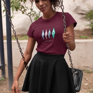 Puede incluir: Una camiseta granate con un gr&aacute;fico de cuatro formas abstractas de colores y el texto "into the unknown".