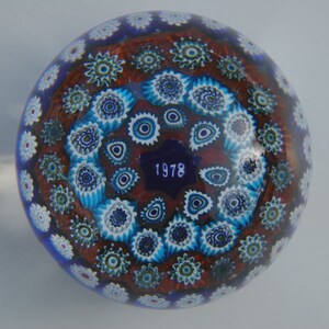 Könnte beinhalten: Ein blauer Glas-Papiergewicht mit einem rot-weiß-blauen Muster. Der Papiergewicht trägt das Datum 1978 auf der Unterseite.