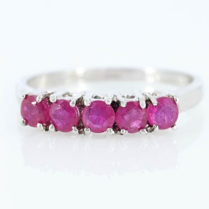 Puede incluir: Un anillo de plata con cinco gemas redondas de color rojo vibrante. Las gemas están engarzadas juntas, creando una línea continua de color. La banda del anillo es de plata pulida, lo que proporciona un aspecto clásico y elegante. Las gemas son de un rojo intenso y rico.