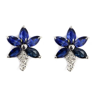 May include: A pair of silver earrings with a flower design. The earrings are made with blue gemstones and clear diamonds.