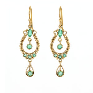 Könnte beinhalten: Goldene Ohrhänger mit smaragdgrünen Edelsteinen. Die Ohrringe haben ein Tropfen-Design mit einem kleineren Tropfen, der von unten herabhängt.