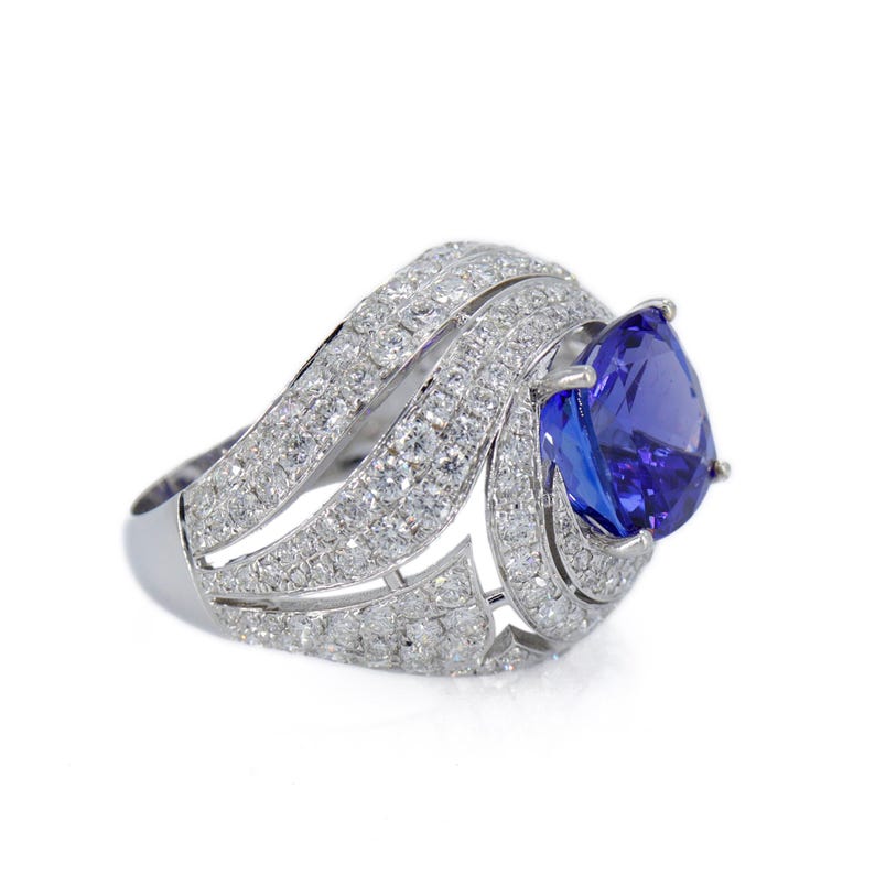 Op de afbeelding: Een oogverblindende ring met een grote, peervormige, diepblauwe edelsteen. De ringband is gemaakt van wit metaal en is bezet met talrijke kleine, sprankelende witte edelstenen, waardoor een halo-effect rond de centrale steen ontstaat. Elegant ontwerp.