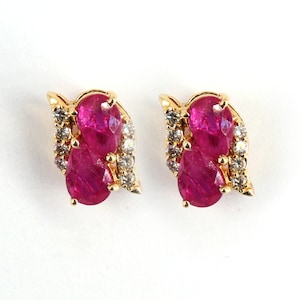 Könnte beinhalten: Ein Paar goldene Ohrringe mit zwei birnenförmigen Rubinen und einem Heiligenschein aus kleinen Diamanten.