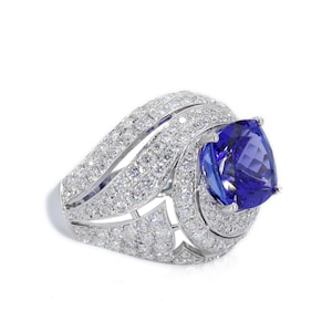 Op de afbeelding: Een oogverblindende witgouden ring met een grote, peervormige, diepblauwe edelsteen. De ring is bezet met talrijke kleine, heldere diamanten, die een halo en band cre&euml;ren. De zetting is ingewikkeld en gedetailleerd.