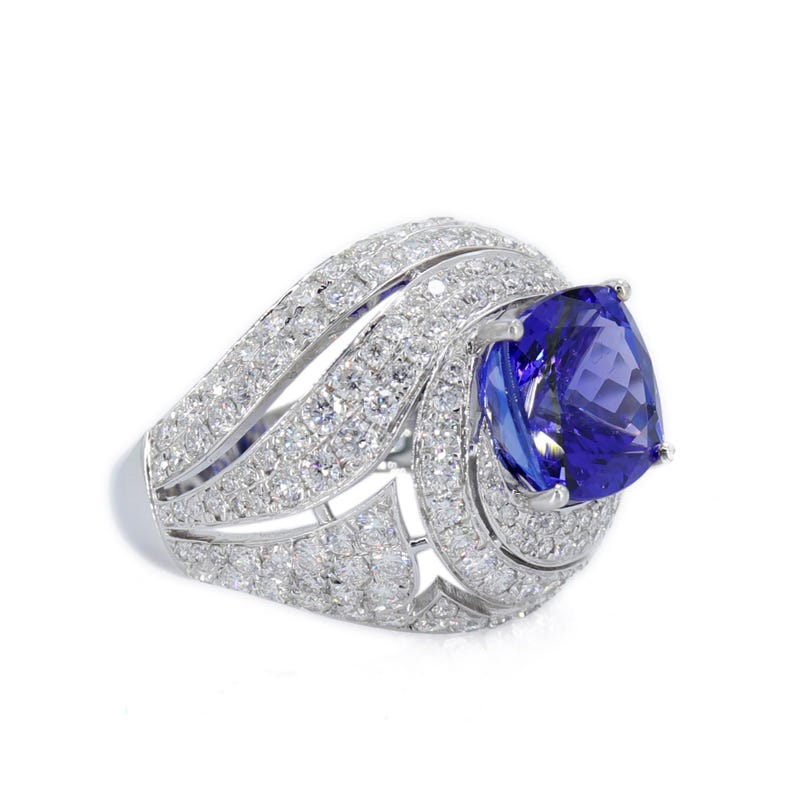 Op de afbeelding: Een oogverblindende witgouden ring met een grote, peervormige, diepblauwe edelsteen. De ring is bezet met talrijke kleine, heldere diamanten, die een halo en band cre&euml;ren. De zetting is ingewikkeld en gedetailleerd.