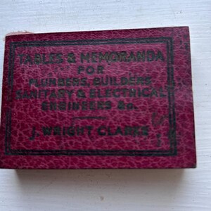 May include: A maroon booklet with the title "TABLES & MEMORANDA FOR PLUMBERS, BUILDERS, SANITARY & ELECTRICAL ENGINEERS &c." in black text. The booklet is by J. Wright Clarke. The text is within a black border.