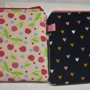 以下が含まれることがあります： ジッパー付きポーチが2つ。1つはベージュの背景にチェリー柄、もう1つは濃い青の背景にハート柄です。