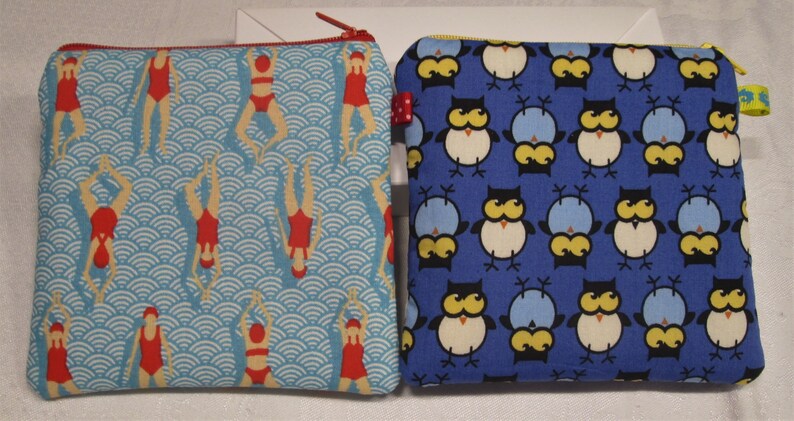 以下が含まれることがあります： 異なるパターンを持つジッパー付きポーチ2つ。1つのポーチは、白い波模様と赤いスイマーが描かれた青色。もう1つのポーチは、白いフクロウ模様が描かれた青色です。