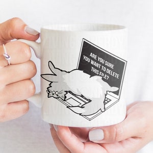 May include: White ceramic mug with a black and white illustration of a cat on a laptop. The laptop screen says "Are you sure you want to delete this file?"
