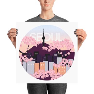 May include: A circular design featuring a cityscape with a tall tower, surrounded by pink cherry blossoms. The text "SEOUL" is written in white against a light blue background.