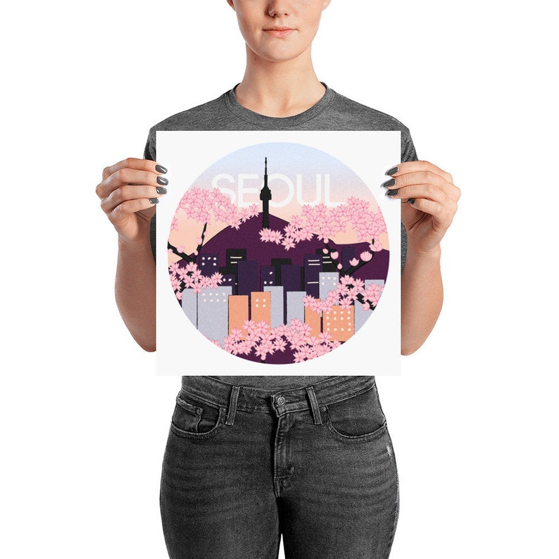 May include: A white poster with a circular design featuring a cityscape silhouette of Seoul, South Korea, with a pink and purple sunset background and cherry blossoms. The text "SEOUL" is written in a bold, black font.