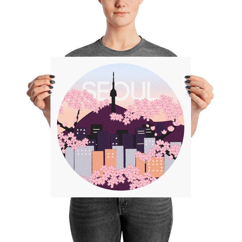 May include: A poster with a circular design featuring a cityscape of Seoul, South Korea, with a tower in the center. The city is surrounded by pink cherry blossoms and the word "SEOUL" is written in white letters.