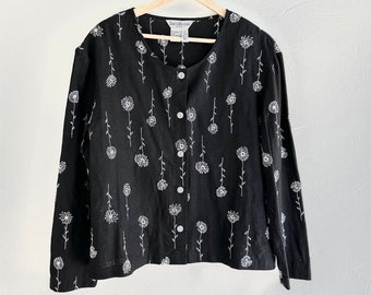 May include: Black long-sleeve button-up shirt with a white daisy print. The shirt has a round neckline and a relaxed fit.