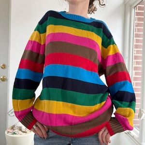 May include: A colorful, striped sweater with a crew neck. The sweater features horizontal bands of various colors, including blue, green, yellow, pink, brown, and red. The sleeves and neckline are trimmed in a solid color, and the sweater appears to be made of a soft knit material.