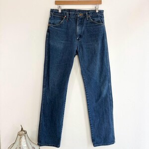 May include: Dark wash denim jeans hanging on a wooden hanger. The jeans have a classic five-pocket design, a button and zipper closure, and a straight leg. The denim is a medium weight, with subtle fading and wear.