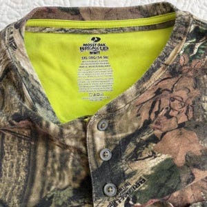 K&ouml;nnte beinhalten: Ein Camouflage-Henley-Shirt mit einem neongr&uuml;nen Kragen. Das Shirt tr&auml;gt den Text "MOSSY OAK BREAK UP INFINITY" und die Gr&ouml;&szlig;e "3XL/3XG (54-56)". Das Shirt besteht aus Baumwolle und Polyester.