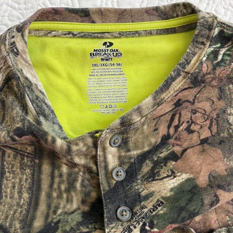 K&ouml;nnte beinhalten: Ein Camouflage-Henley-Shirt mit einem neongr&uuml;nen Kragen. Das Shirt tr&auml;gt den Text "MOSSY OAK BREAK UP INFINITY" und die Gr&ouml;&szlig;e "3XL/3XG (54-56)". Das Shirt besteht aus Baumwolle und Polyester.