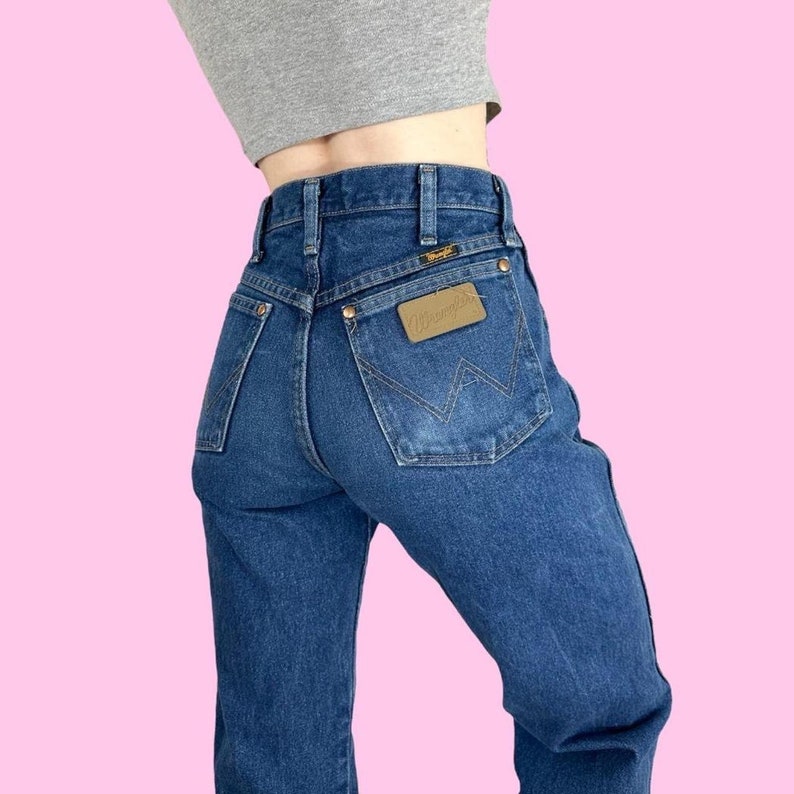 Puede incluir: Un par de pantalones vaqueros azules con un parche de cuero marr&oacute;n en el bolsillo trasero que dice "Wrangler".