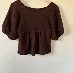 May include: A brown knitted sweater with a scoop neck and short puff sleeves.